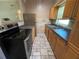 Galley kitchen featuring wooden cabinetry, black appliances, stainless refrigerator, and tile flooring at 1703 Doreen Ave, Ocoee, FL 34761