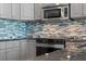 Modern kitchen appliances with grey cabinets, black granite countertops, and mosaic tile backsplash at 101 S Eola Dr # 1001, Orlando, FL 32801