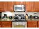 Close-up view of stainless steel appliances, including a range, microwave, and cooktop, set against wooden cabinetry at 5025 Shoreway Loop # 20503, Orlando, FL 32819