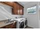 Bright laundry room with window, sink, countertop, and modern, front-loading washer and dryer units at 3443 Players Point Loop, Apopka, FL 32712