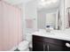 Well-lit bathroom with a single sink vanity, toilet, shower with pink curtain, and a large mirror at 13875 Sachs Ave, Orlando, FL 32827