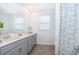 Well-lit bathroom features a double sink vanity with grey cabinetry and a decorative seashell shower curtain at 1920 Perch Hammock Loop, Groveland, FL 34736