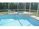 Sparkling blue in-ground pool with adjacent jacuzzi surrounded by a screened enclosure and view of forest in the background at 2989 Viscount Cir, Kissimmee, FL 34747