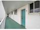 Exterior condo hallway with white walls, windows, and door painted in seafoam green leading to the unit entrance at 2727 N Atlantic Ave # 2020, Daytona Beach, FL 32118