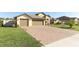 Paver driveway leads to a two-car garage on a light yellow house with manicured lawn at 9716 Royal Vista Ave, Clermont, FL 34711