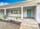 Close up view of the front porch with tile flooring, a teal front door and colorful plants in a flower bed at 1510 Live Oak St, New Smyrna Beach, FL 32168