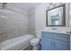 Well-lit bathroom features a tub with gray tiled walls and a blue vanity with white countertop at 2540 Woodgate Blvd # 106, Orlando, FL 32822