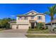 Two-story tan home with brick driveway, three-car garage, stone accents, manicured lawn, and lovely landscaping at 5142 Sage Cedar Pl, Sanford, FL 32771