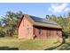 A rustic red barn is equipped with solar panels for sustainable energy, set in a green, tree-filled area at 11811 Kijik Trl, Groveland, FL 34736