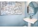 Stylish powder room with a pedestal sink, round mirror, and elegant artwork at 7821 Waterscape Dr, Groveland, FL 34736