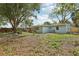 A spacious backyard with green grass, scattered leaves, mature trees and a charming light blue painted home at 5215 Ashwood Pl, Orlando, FL 32808