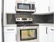 Close-up of stainless steel oven and microwave with white cabinets and grey subway tile backsplash at 5443 Aeolus Way, Orlando, FL 32808