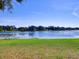 Lakeside view featuring grassy yard with a tree-lined backdrop under a clear blue sky at 2055 Jessamine Ct, Deltona, FL 32738