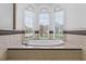 Elegant soaking tub with tile surround and three arched windows offering a view of the outdoors at 674 Whisper Woods Dr, Lakeland, FL 33813