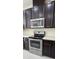 Close-up view of stainless steel microwave and oven with dark wood cabinets and white subway tile backsplash at 15471 Honeybell Dr, Winter Garden, FL 34787