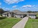 Stunning single-story home featuring a long driveway, mature landscaping, and a classic facade with arched windows and entryway at 15523 Trotting Horse Ln, Tavares, FL 32778