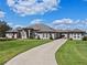 Gorgeous single-story home featuring a long driveway, manicured lawn, and a grand facade with arched windows and entryway at 15523 Trotting Horse Ln, Tavares, FL 32778