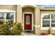 Close-up of a red front door with decorative glass, flanked by windows and lush green shrubbery at 639 Mesilla Dr, Kissimmee, FL 34758