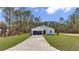 A modern one-story home with a long driveway and a well-maintained lawn surrounded by tall trees at 7117 Sw 131St Ave, Ocala, FL 34481