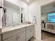 Bright bathroom featuring double vanity with granite countertop and grey cabinets, plus a glimpse into an adjacent bedroom at 3764 Shoveler Ave, Leesburg, FL 34748