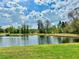 View of a calm, reflective pond surrounded by green grass and trees under a bright sky at 17519 Blessing Dr, Clermont, FL 34714