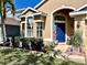 Close up of a home's facade showing manicured landscaping with mature plants flanking an arched blue front door at 2707 Barnsley Ln, Kissimmee, FL 34744