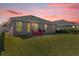 Twilight backyard view of patio with red chairs, well-maintained lawn, and exterior elevation of the home at 1200 Kellogg Dr, Tavares, FL 32778