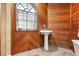 Cozy bathroom features a pedestal sink, custom wood walls, and arched window at 1500 Whitstable Ct, Lake Mary, FL 32746