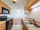 Functional kitchen featuring black appliances, light wood cabinets, and a double basin sink at 1695 Lee Rd # E205, Winter Park, FL 32789