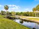Scenic waterfront view featuring a dock, calm water reflecting the sky, and lush landscaping with palm trees at 1475 Warrior Trl, Enterprise, FL 32725