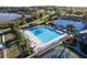 Aerial view of a large community pool surrounded by lush landscaping, tennis courts, and tropical palms at 5025 St Andrews Arc, Leesburg, FL 34748