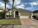 Charming home showcasing tropical landscaping, a brick driveway, and an attached two-car garage at 1923 Willow Wood Dr, Kissimmee, FL 34746