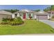 Charming single-story home with a well-manicured lawn, vibrant landscaping, and a striking red front door at 24515 Bocage Way, Leesburg, FL 34748