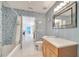Bright bathroom features unique blue patterned walls, a shower-tub, and wood vanity, and a door to other parts of the home at 5170 Ne 64Th Ave, Silver Springs, FL 34488