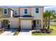 Two-story tan townhome featuring an attached garage, lush lawn, and a vibrant palm tree at 10849 Wyne Tree Ct, Orlando, FL 32824