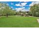 Expansive backyard with manicured lawn, pool, lounge chairs, tiki umbrellas, lush landscaping, and shade trees at 8244 Oakland Pl, Orlando, FL 32819