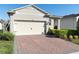 Beige two-car garage on a charming home with a brick driveway and neatly manicured landscaping at 17398 Blazing Star Cir, Clermont, FL 34714