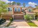 Front view of the townhome with well manicured landscaping and a three-car garage with brick driveway at 4952 Matteo Trl, Orlando, FL 32839