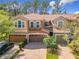 Exterior view of townhome highlighting a three-car garage, brick driveway, and lush tropical landscape at 4952 Matteo Trl, Orlando, FL 32839