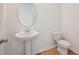 Half bath with a pedestal sink and oval mirror with wood-look floors and white walls at 5719 Cattle Ranch Dr, St Cloud, FL 34771