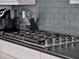 Close up of stainless steel gas cooktop on an island with shaker style cabinets and grey backsplash at 1281 Grand Traverse Pkwy, Reunion, FL 34747