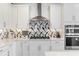 Close-up of a modern kitchen featuring white cabinets, stainless steel appliances, and stylish backsplash at 13916 Destin Beach Ln, Orlando, FL 32827
