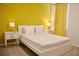 Bright bedroom with yellow accent wall, white bedding, bedside tables and lamps, modern minimalist style at 4489 Monado Dr, Kissimmee, FL 34746