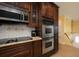 Close-up of a kitchen area with dark wood cabinets, stainless steel double oven, granite counters and a yellow wall at 504 Teakwood Dr, Altamonte Springs, FL 32714