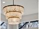 Close-up of a modern, three-tiered chandelier with natural light filtering through nearby windows at 10148 Chiltern Garden Dr, Orlando, FL 32827