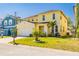 Inviting two-story yellow home with a well-manicured lawn, palm trees, and a two-car garage at 277 Sand Ridge Dr, Davenport, FL 33896