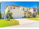 Charming two-story yellow home with a well-manicured lawn, palm trees, and a two-car garage at 277 Sand Ridge Dr, Davenport, FL 33896