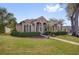 Single-story tan home featuring a manicured lawn, decorative shutters, and palm trees at 1415 Crocus Ct, Longwood, FL 32750