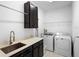 Functional laundry room featuring a stainless steel sink, dark cabinets, and modern washer and dryer at 2145 Rush Bay Way, Orlando, FL 32824