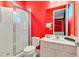 Vibrant red bathroom with glass shower, toilet, white vanity, and framed mirror, offering a stylish and functional space at 1468 Fairview Cir, Reunion, FL 34747